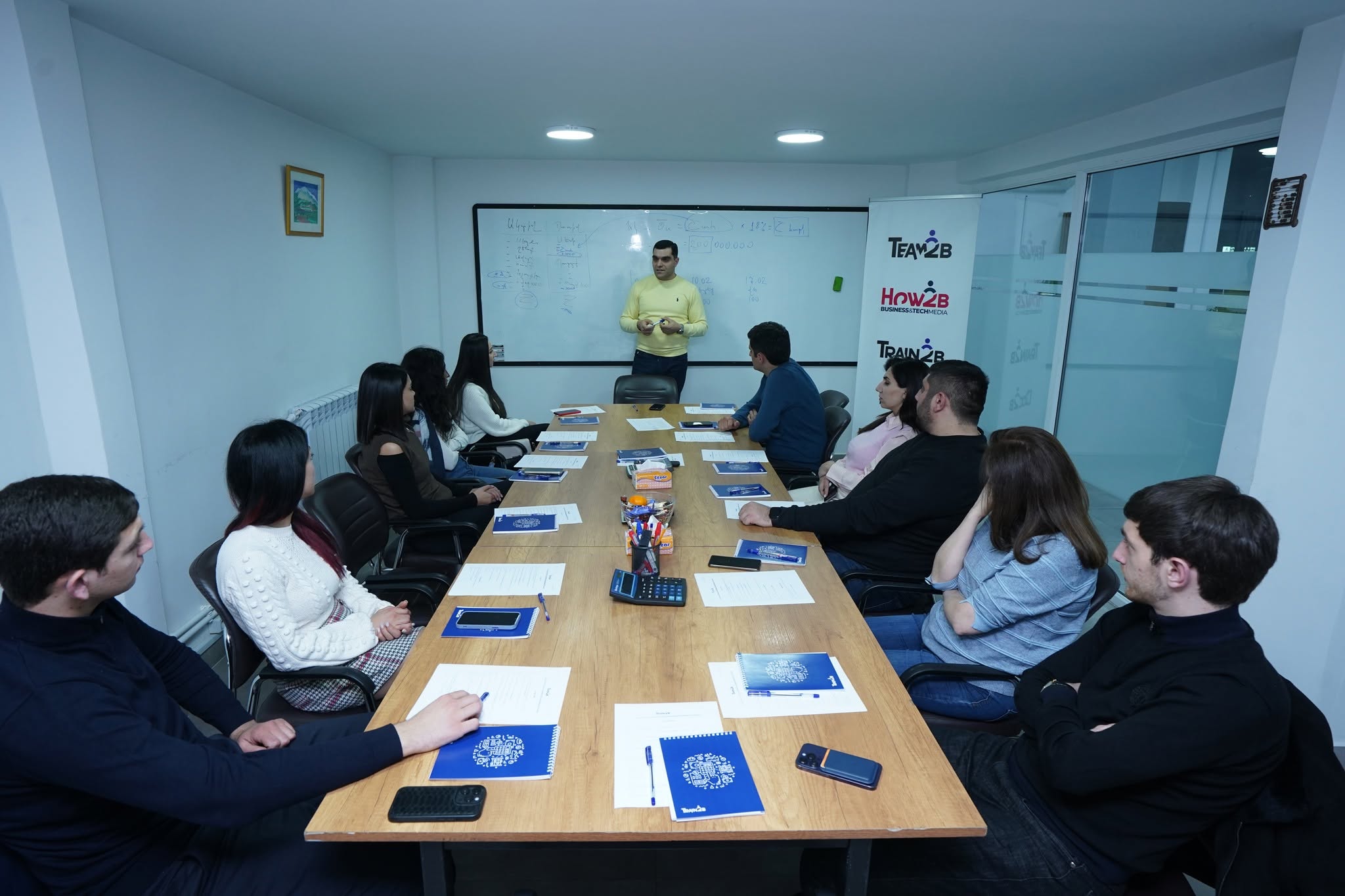 A real Train2b instructor teaching at a whiteboard with a group of adult students in a classroom
